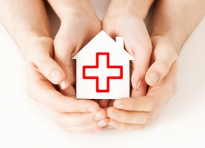 hands holding paper house with red cross